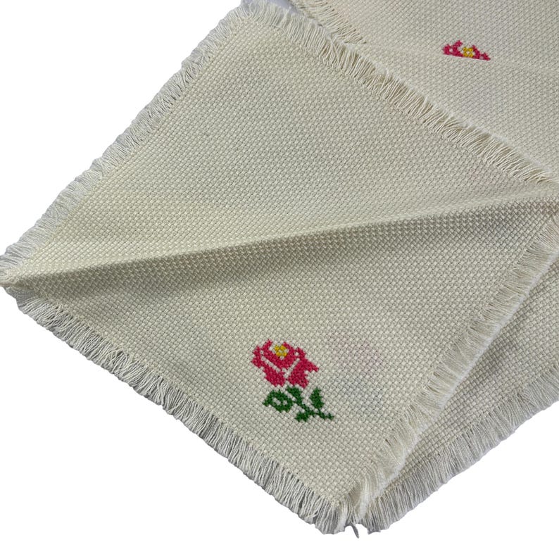 May include: Two white linen napkins with embroidered red roses. The napkins have a fringed edge.