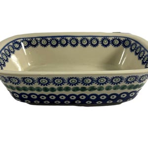 May include: A white ceramic baking dish with a blue and green geometric pattern. The dish has a rectangular shape with rounded corners.