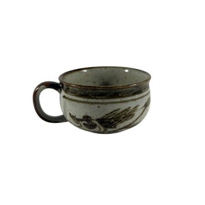 May include: A wide, low-profile ceramic mug with a speckled light gray finish. The exterior features a dark brown band around the rim and a dark brown hand-painted bird motif. It has a curved, dark brown handle and a wide, open circular mouth.
