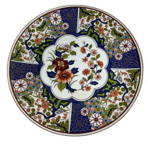 May include: A round, decorative plate with a floral design. The plate features a white center with a floral arrangement in shades of red, orange, and green. The border is a deep blue with gold accents and additional floral patterns. The plate has a gold rim.