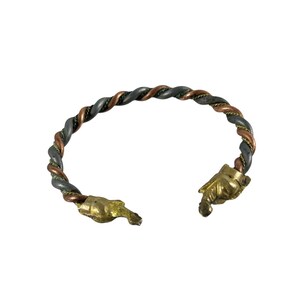 May include: A twisted metal bracelet with a mix of gray, copper, and gold tones. The bracelet features a braided design and is open-ended, with gold-colored hand-shaped terminals. The overall style is rustic and artistic.