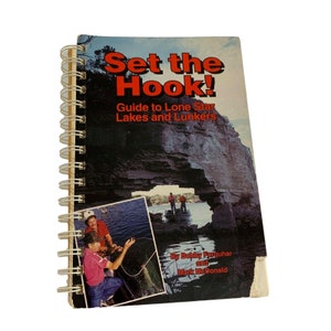 May include: A spiral bound book titled "Set the Hook! Guide to Lone Star Lakes and Lunkers" by Bobby Farquhar and Mark McDonald. The cover features a photo of a rocky archway over a lake with two people fishing in the distance.