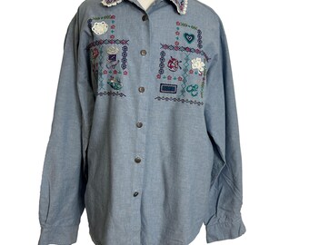 May include: A light blue denim button-up shirt with embroidered details. The embroidery features a variety of colorful designs, including flowers, hearts, and geometric patterns.