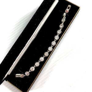 May include: A silver bracelet with a row of clear round stones. The bracelet is in a black velvet box.