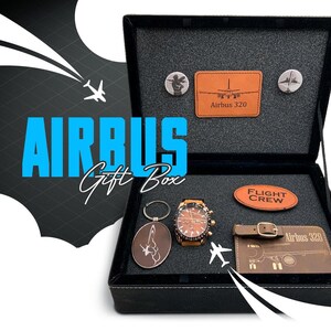May include: A black gift box with a blue "AIRBUS Gift Box" inscription on the front. The box is open and contains a watch, a keychain, a leather patch with the text "FLIGHT CREW", and a brown leather patch with the text "Airbus 320".