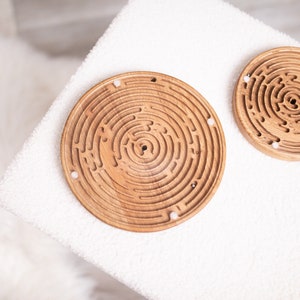 Könnte beinhalten: Zwei runde Holz-Labyrinthspiele mit weißen Murmeln. Die Labyrinthe sind aus hellbraunem Holz gefertigt und haben ein kreisförmiges Design.
