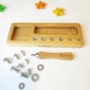 May include: Wooden toy workbench with a screwdriver and various screws, nuts, and washers. The workbench has two compartments and is engraved with the name "Aaron".