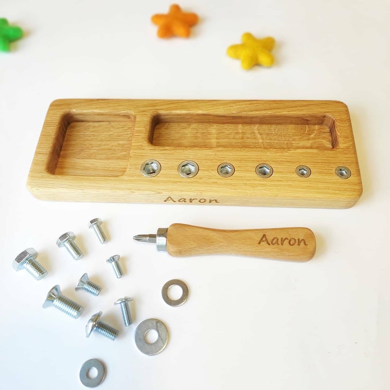 May include: Wooden toy workbench with a screwdriver and various screws, nuts, and washers. The workbench has two compartments and is engraved with the name "Aaron".