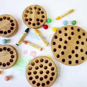 May include: A set of four wooden circular trays with various sized holes. The trays are made of light brown wood and are perfect for sorting and organizing small items. The trays are surrounded by colorful felt balls and crayons.