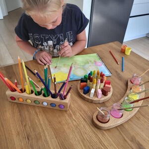Puede incluir: Un portal&aacute;pices rectangular de madera con incrustaciones circulares de colores, un bloque de madera circular que sostiene crayones en posici&oacute;n vertical y una bandeja de madera curva con cinco frascos de vidrio peque&ntilde;os llenos de pintura l&iacute;quida.