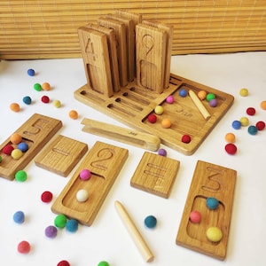 Puede incluir: Juguete de aprendizaje de n&uacute;meros de madera con una bandeja, 10 bloques de madera con los n&uacute;meros del 1 al 10 y pompones de colores. La bandeja tiene una ranura para cada bloque de n&uacute;mero y un peque&ntilde;o palo de madera. El juguete est&aacute; etiquetado con "Jae".