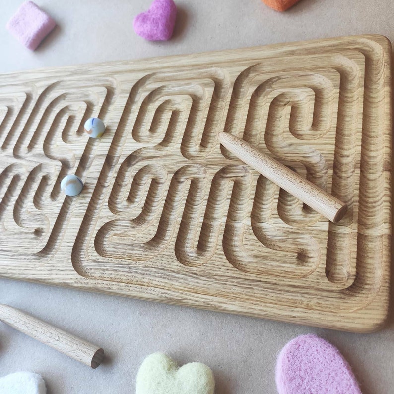 May include: A wooden maze game with two white marbles and a wooden stick to move the marbles. The maze is made of oak wood and has a natural finish.