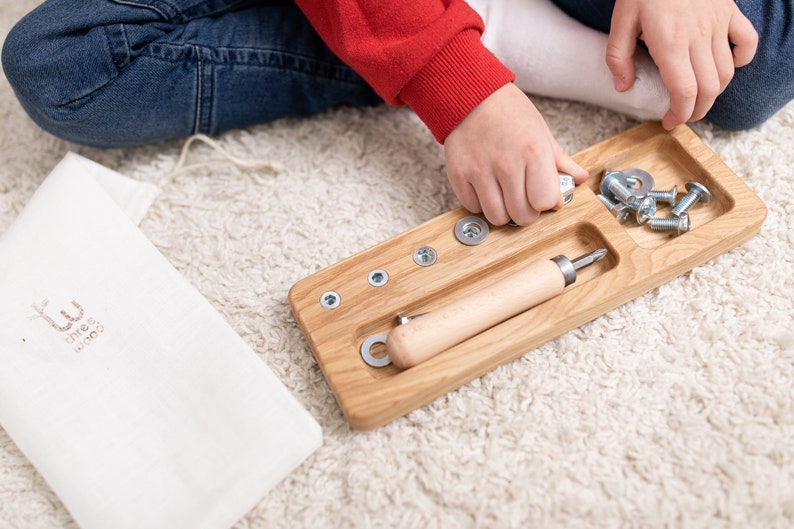 May include: A wooden tray with compartments for screws, nuts, and a screwdriver. The tray is made of light wood and has a natural finish. The screws and nuts are silver and the screwdriver has a wooden handle.