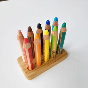 May include: A collection of colorful pencils in a wooden holder. The pencils are various colors, including red, orange, yellow, green, blue, and black. The pencils are arranged upright in a rectangular wooden base.