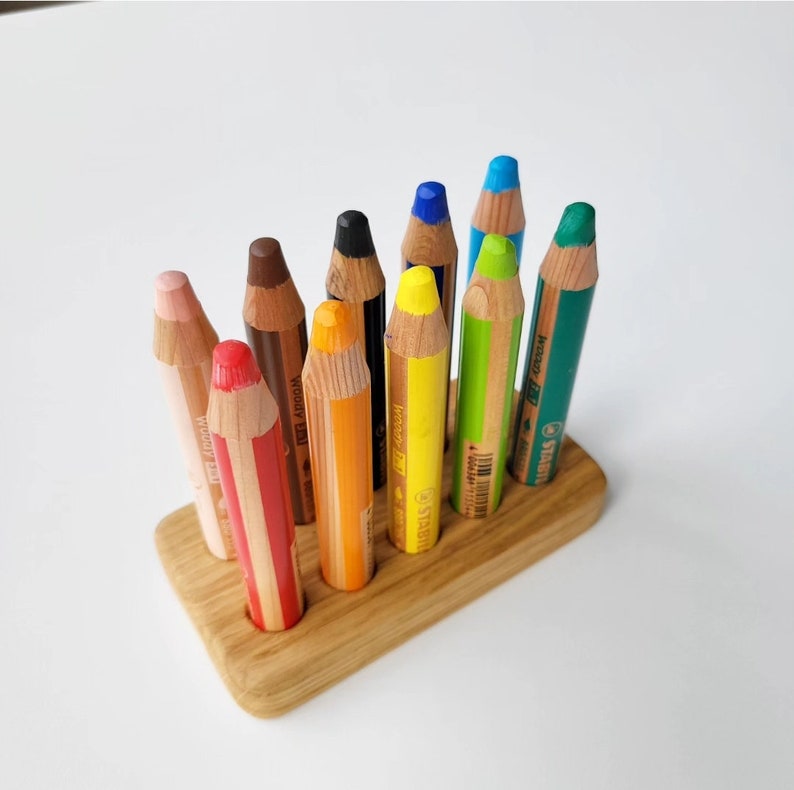 May include: A collection of colorful pencils in a wooden holder. The pencils are various colors, including red, orange, yellow, green, blue, and black. The pencils are arranged upright in a rectangular wooden base.