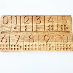 May include: Wooden number tracing board with numbers 0-10 carved into the surface. Each number has a corresponding number of dots below it. The board is made of light brown wood and is designed for educational purposes.