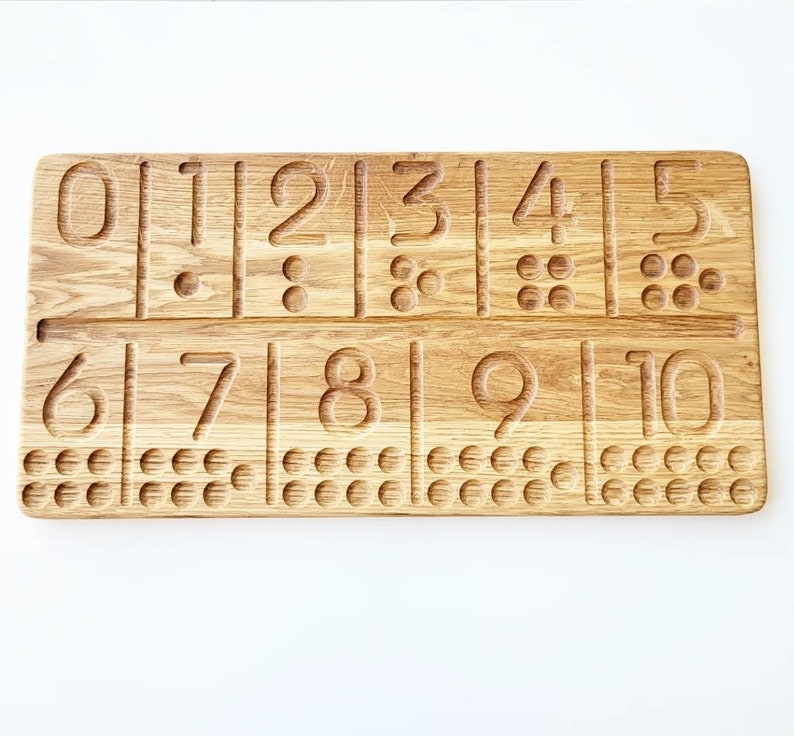 May include: Wooden number tracing board with numbers 0-10 carved into the surface. Each number has a corresponding number of dots below it. The board is made of light brown wood and is designed for educational purposes.