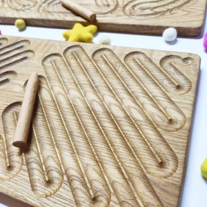 May include: Wooden tracing board with a series of curved lines for tracing with a wooden dowel. The board is light brown with a natural wood grain.