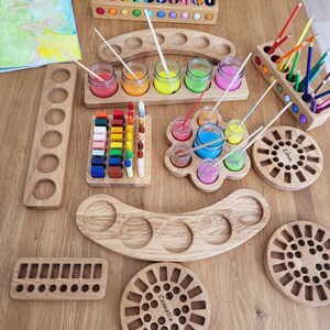 Puede incluir: Una colecci&oacute;n de organizadores de arte de madera clara, que incluye portal&aacute;pices rectangulares y curvos, bandejas para botes de pintura y tableros circulares con orificios tallados. Algunos tableros tienen grabados los nombres Linn y Camelia.