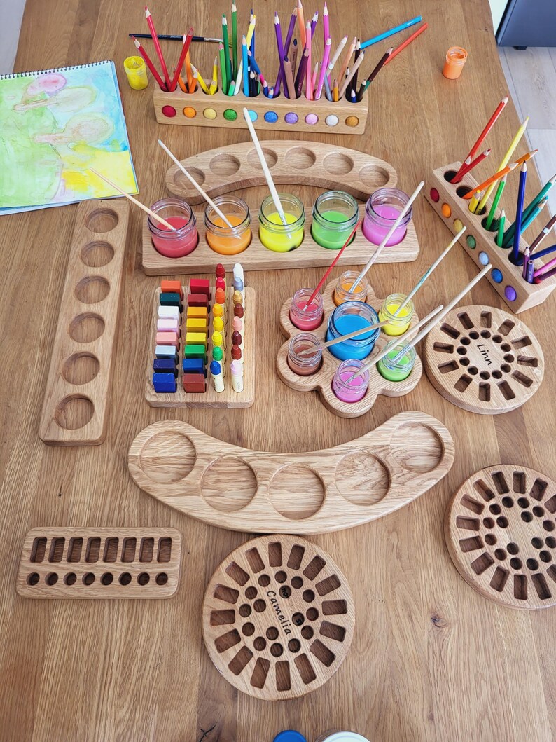 Puede incluir: Una colecci&oacute;n de organizadores de arte de madera clara, que incluye portal&aacute;pices rectangulares y curvos, bandejas para botes de pintura y tableros circulares con orificios tallados. Algunos tableros tienen grabados los nombres Linn y Camelia.
