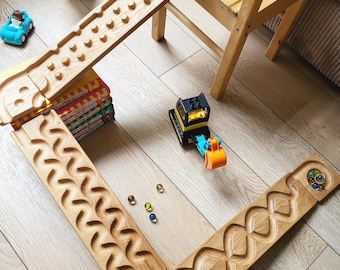 May include: Wooden marble run with a variety of track designs, including a zig-zag and a series of pegs. A blue toy car, a yellow and black toy excavator, and marbles are on the track. A stuffed animal and a wooden chair are also in the scene.