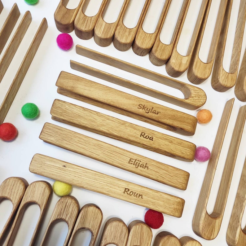Puede incluir: Bloques de madera de juguete con nombres grabados en ellos. Los bloques est&aacute;n dispuestos en una fila con bolas de colores esparcidas a su alrededor. Los nombres en los bloques son Skylar, Roa, Elijah y Roun.