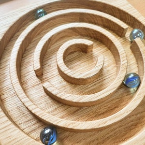 May include: A wooden maze with a circular design and four glass marbles. The marbles are blue, green, and clear.