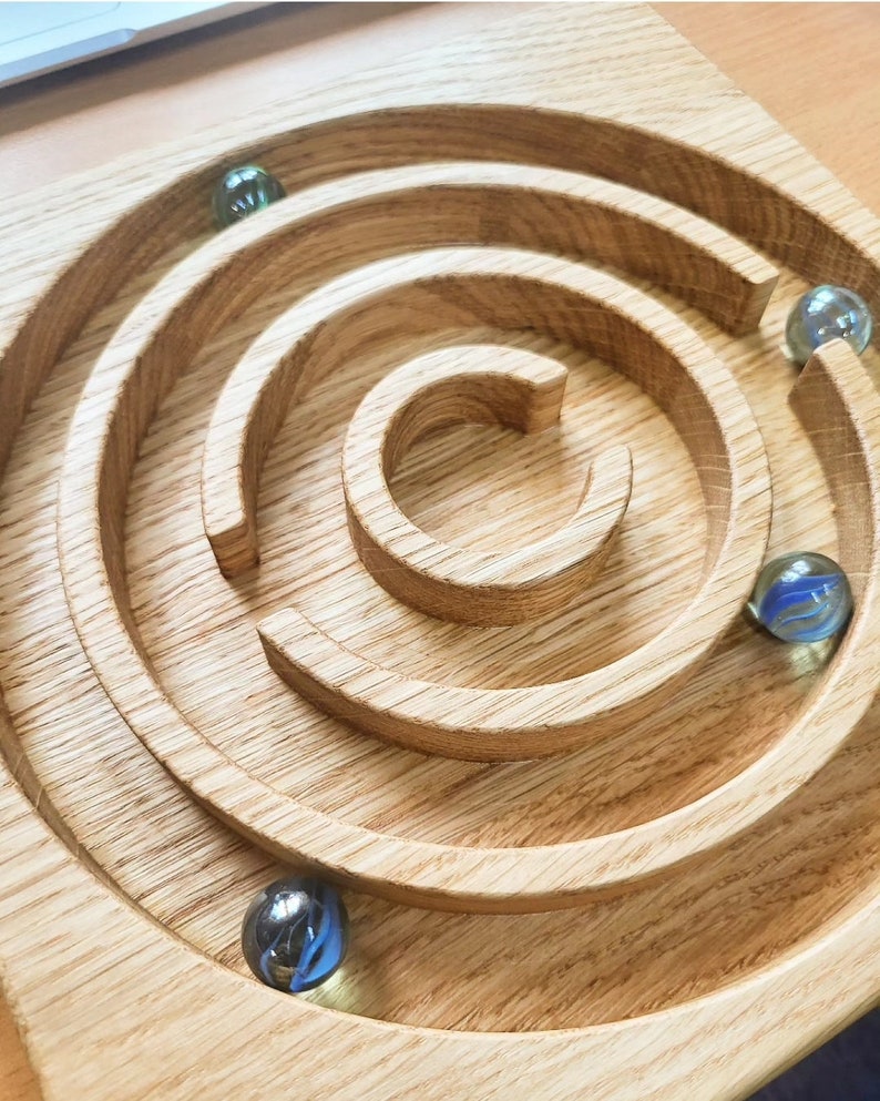 May include: A wooden maze with a circular design and four glass marbles. The marbles are blue, green, and clear.