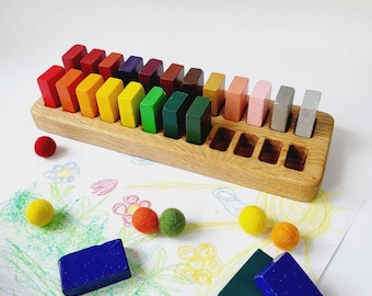 Könnte beinhalten: Holz-Stifthalter mit einem Regenbogen aus Buntstiften in verschiedenen Farben. Der Halter besteht aus hellem Holz und hat mehrere Schlitze zur Aufnahme der Stifte. Der Text "crayons not included" ist sichtbar.