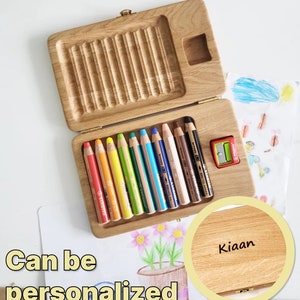 May include: Wooden pencil case with a hinged lid, containing a set of colourful pencils and a pencil sharpener. The case is open, revealing the pencils in various colours. The text "Can be personalised" is visible.