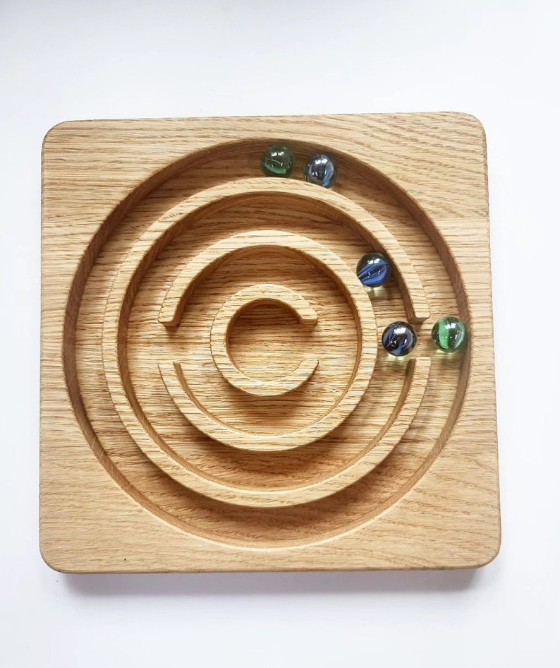 May include: A wooden marble run game with a circular track and multiple levels. Four marbles, two green and two blue, are in the track.
