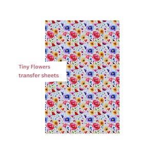 Könnte beinhalten: Ein Blatt farbiges Transferpapier mit einem Muster aus kleinen Blumen in den Farben Rosa, Gelb, Blau und Lila auf weißem Hintergrund. Der Text "Tiny Flowers transfer sheets" ist auf das Blatt gedruckt.