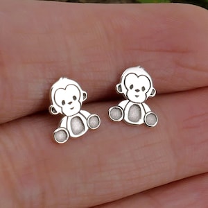 Può includere: Un paio di orecchini a perno in argento a forma di scimmia. Le scimmie sono sedute con le braccia distese e hanno un design semplice e cartonato.