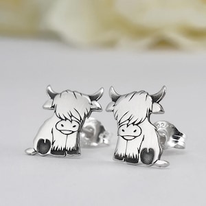 Puede incluir: Un par de pendientes de plata con un diseño de vaca Highland de estilo de dibujos animados. Los pendientes son pequeños y delicados, perfectos para el uso diario.