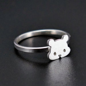 May include: A silver ring with a bear face design. The ring is simple and minimalist.