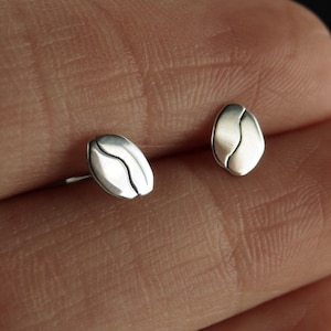 May include: A pair of silver coffee bean stud earrings. The earrings are small and delicate, and they are perfect for everyday wear.