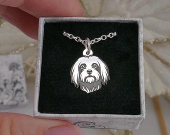 May include: A silver pendant necklace featuring a detailed Maltese dog face. The pendant is displayed in a small, open gift box with a black interior. The necklace chain is also silver.