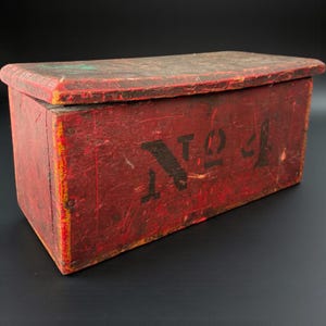 Peut inclure: Une boîte en bois rouge vieillie avec un couvercle incurvé. La boîte porte le numéro "No. 4" pochoir en noir sur le devant. La peinture est usée, montrant des signes d'âge, lui donnant un aspect rustique.
