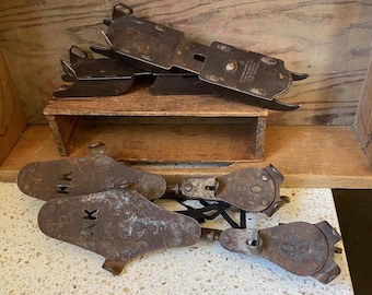 May include: A set of antique ice skates with metal blades and leather straps. The skates are rusty and have a worn patina. The blades are marked with the letters "HK".