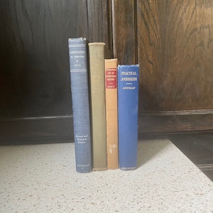 Puede incluir: Una pila de cuatro libros de tapa dura con cubiertas azules, verdes, naranjas y azules. Los títulos son "Composers in America", "The Structure of Music", "International Law and Relations", y "Practical Journalism".