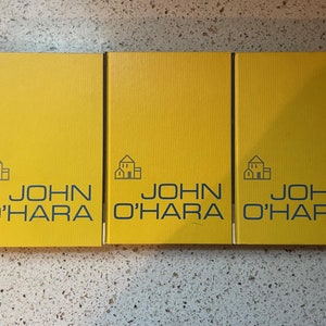 May include: Three yellow hardcover books with the title "JOHN O'HARA" and a small house icon on the front cover.