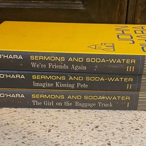 May include: A stack of three yellow paperback books with the title "Sermons and Soda-Water" by John O'Hara. The books are numbered I, II, and III. The books are published by Random House.