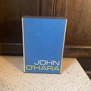 May include: A blue and black box with the text "JOHN O'HARA" in yellow letters.