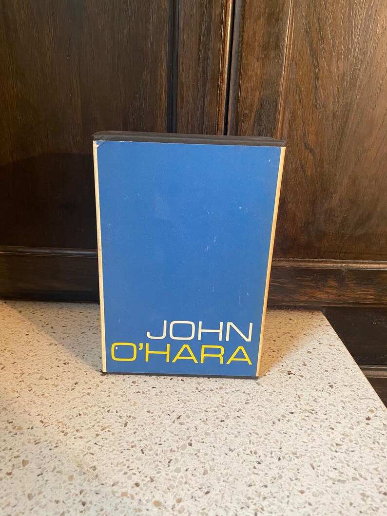 May include: A blue and black box with the text "JOHN O'HARA" in yellow letters.