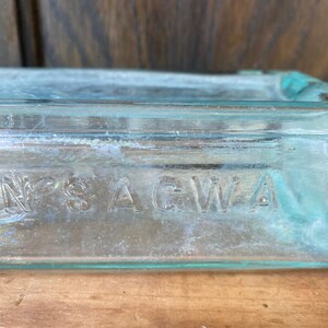Puede incluir: Primer plano de una botella de vidrio transparente con la palabra "SAGWA" grabada en el lateral.