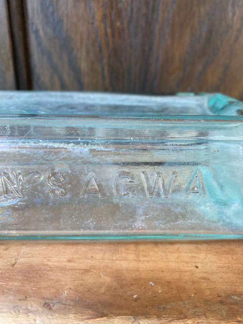 Puede incluir: Primer plano de una botella de vidrio transparente con la palabra "SAGWA" grabada en el lateral.