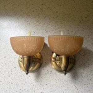 Könnte beinhalten: Ein Paar Wandleuchten mit halbkreisförmigen, mattierten pfirsichfarbenen Glasschirmen mit geprägtem Blumenmuster. Jeder Schirm wird von einem metallischen, messingfarbenen Sockel mit einem zentralen Arm und einer runden Wandplatte gehalten.