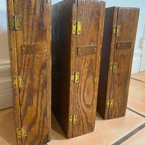 May include: Three vertical wooden storage boxes with a dark brown wood grain finish. Each box features brass hinges and a small brass label plate. The labels are engraved with the words INSURE, RECEIPT, and MAIL respectively in capital letters.