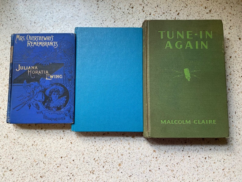K&ouml;nnte beinhalten: Drei antike gebundene B&uuml;cher mit blauen, gr&uuml;nen und gr&uuml;nen Einb&auml;nden. Das Buch links tr&auml;gt den Titel "Mrs. Overtheway's Remembrances" und den Autor "Juliana Horatia Ewing" mit Illustrationen. Das mittlere Buch hat einen einfarbigen blauen Einband. Das Buch rechts tr&auml;gt den Titel "Tune-In Again" und den Autor "Malcolm Claire".