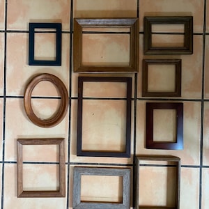 May include: A collection of empty picture frames in various shapes and sizes. The frames are made of wood and have different finishes, including dark brown, light brown, and gray. One frame is oval-shaped.